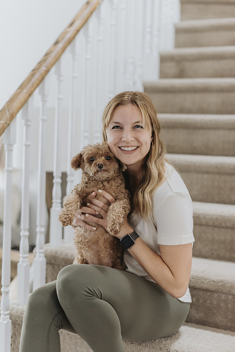 female Smiling woman holding cute poodle while sitting on steps at home