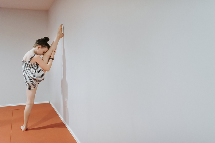 female Girl stretching legs by white wall at home