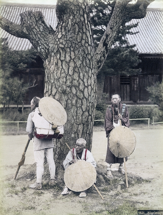 Pilgrim  unknown date  Three Pilgrims are resting at a weathered pine tree in what appears to be the grounds of a buddhist temple. They are wearing white vestments, sugegasa  sedge woven hats  and waraji  straw sandals . They are also holding long walking sticks and carry primitive backpacks. The pilgrim on the right carries a juzu  buddhist rosary  around his neck. The sugegasa have the characters for  kin   gold  and  dougyou   fellow pilgrim  written on it, which indicates that they are on a pilgrimage to Kotohira gu shrine, better known as Konpira san, in Kagawa Prefecture.