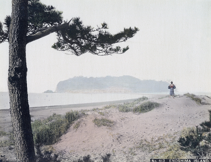 Enoshima Island  unknown date  The island of Enoshima in Sagami Bay, Kanagawa Prefecture as seen from the dunes on shore. A reach of sand stretching from the beach to the island can be seen to the left of the man with his back to the camera. The tiny island with a circumference of just 4 km was connected to the mainland during low tide, but could only be reached by boat during high tide.