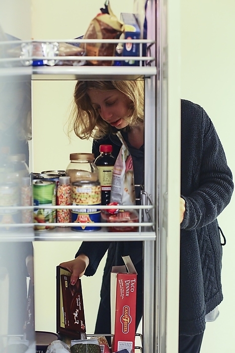 Young woman with a food craving Young woman with a food craving goes through her pantry looking for a snack