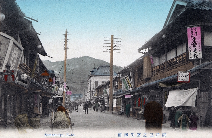 Sannomiya, Kobe  shooting date unknown  This postcard of Sannomiya in Kobe, Hyogo Prefecture shows Ikuta mae, the street leading to the shinto shrine Ikuta Jinja. In the background the shrine s torii can be seen. One Western style building made of stone stands out among the otherwise traditional wooden architecture. Kobe opened its port for trade in 1868  Meiji 1 , this was a beautiful sand road that lead from the shrine to the sea and was lined on both sides with plum and cherry trees and countless stone lanterns. When its port for trade in 1868  Meiji 1 , this was a beautiful sand road that lead from the shrine to the sea and was lined on both sides with plum and cherry trees and countless stone lanterns.