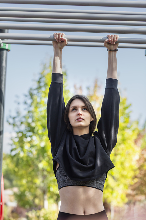 female Fit young woman hanging from monkey bars at playground, by Vladimir Godnik