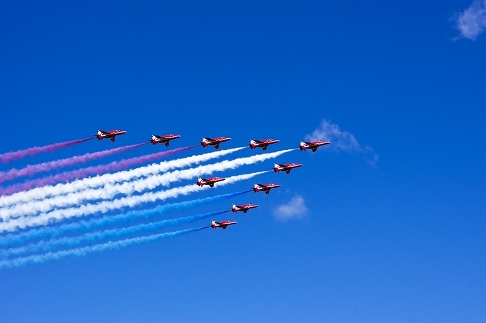 The Red Arrows. The Red Arrows, officially known as the UK Royal Air Force Aerobatic Team, displaying over southern England. The 10 Hawk Trainers are shown flying in formation against a blue sky trailing red, white and blue smoke.