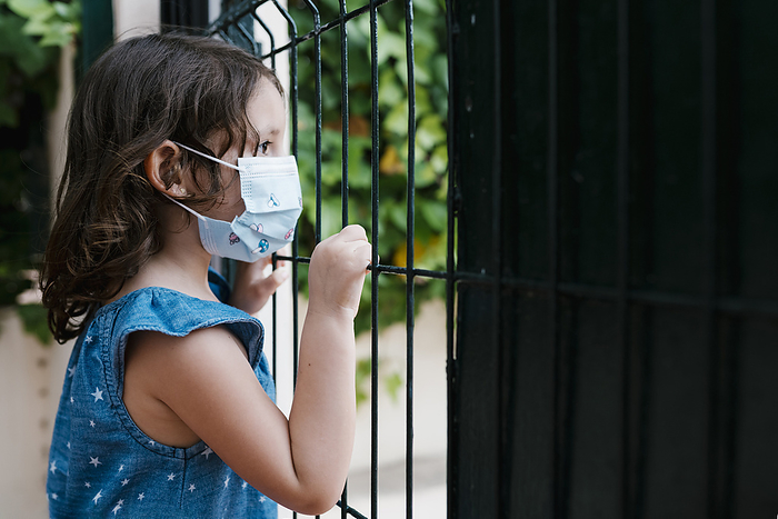 Close-up of girl wearing mask looking through fence while standing in yard