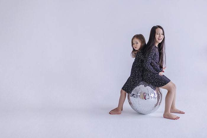 Girls smiling while sitting on silver ball against white background in studio