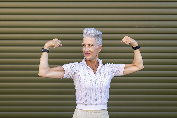Senior Woman Senior woman flexing muscles while standing against shutter