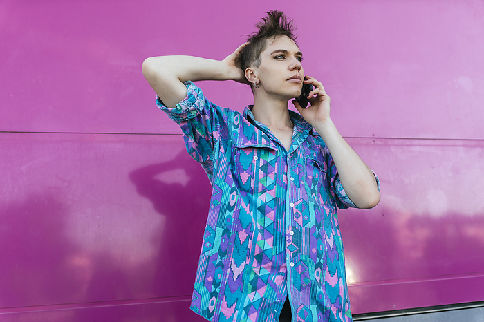 masculine gender Non binary person talking on mobile phone while standing against pink wall