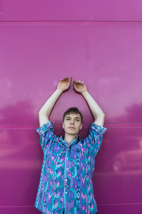 masculine gender Non binary person with hand raised standing against pink wall