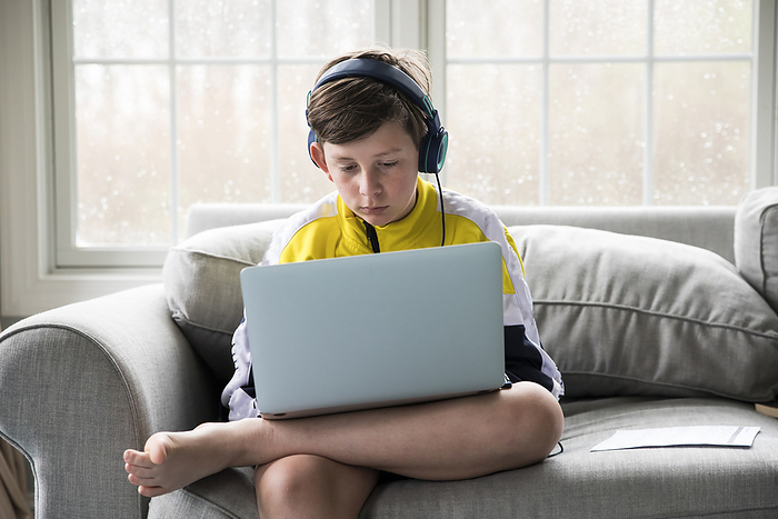 child Tween Boy Using Laptop for Virtual School Sits on Living Room Couch