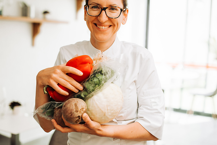 Female chef smiling at camera while holding fresh vegetables