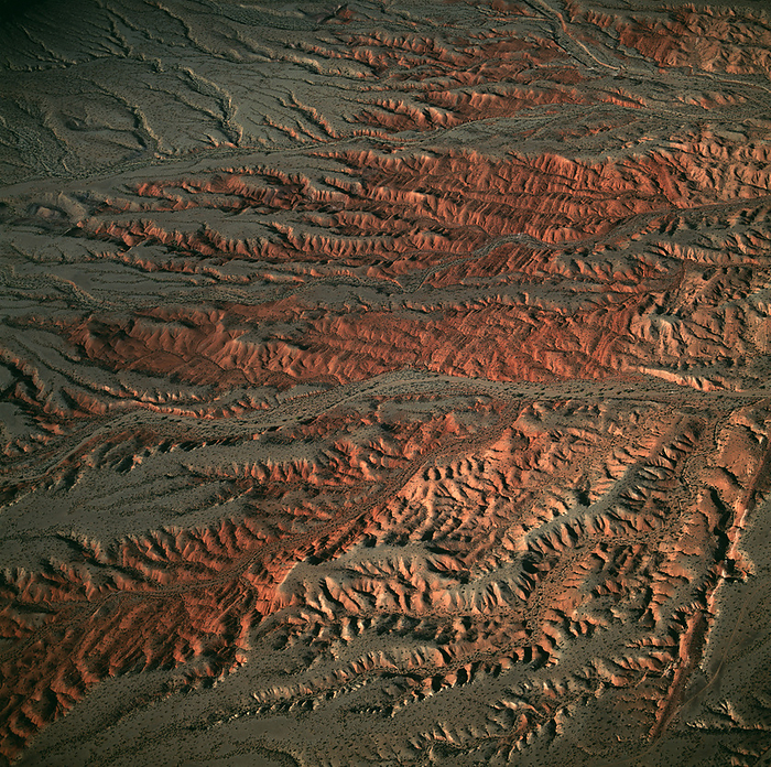 Eroded landscape Eroded landscape. Aerial photograph showing rock formations in the semi desert area of Nevada, USA. Erosion of the grey surface layer by wind and rare rainfalls have exposed red rock. Rubble  black  has been deposited along channels that are rivers during wet periods. Harder ribs in the red rock are seen as parallel stripes.