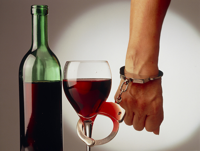 Abstract representation of alcohol dependence Alcohol dependence. A person handcuffed to a glass of wine. This is an illness characterised by habitual, compulsive, long term consumption of alcohol and the development of withdrawal symptoms when drinking is suddenly stopped. Physical symptoms related to it include nausea, vomiting, abdominal pain, cramps, irregular pulse, redness and enlarged capillaries in the face. Many alcoholics require detoxification which is followed by long term treatment.