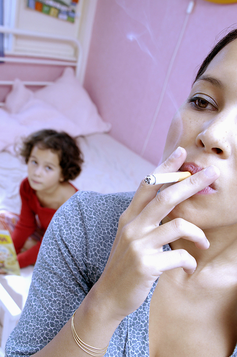 Woman smoking MODEL RELEASED. Woman smoking with a six year old girl reading in the background. Cigarette smoke creates an unhealthy atmosphere for children.