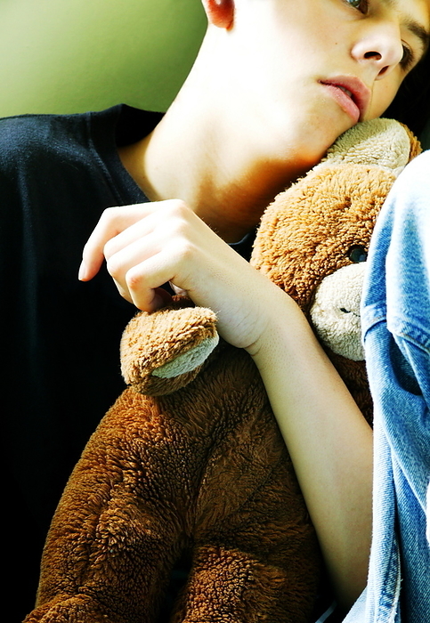 Child abuse Child abuse. Teenage boy sitting in a corner cuddling a teddy bear.