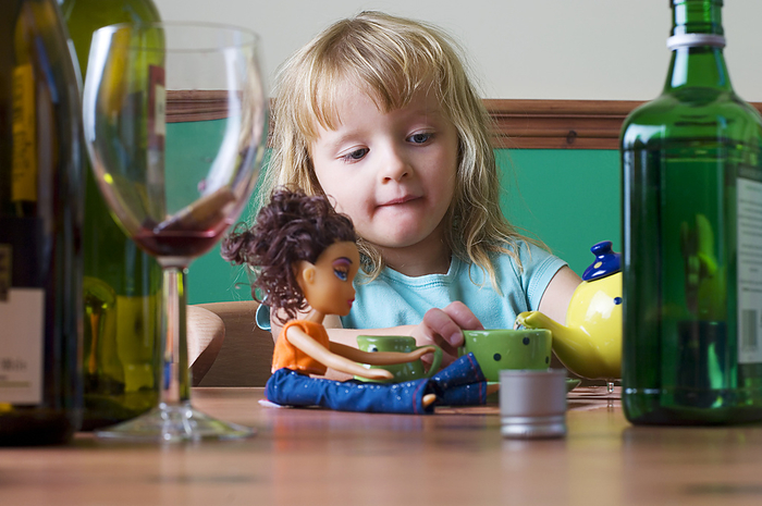 Child neglect MODEL RELEASED. Child neglect, conceptual image. Young girl having a tea party with her dolly, surrounded by bottles of alcohol and an empty wine glass. This could represent child neglect due to a parent s dependancy on alcohol.