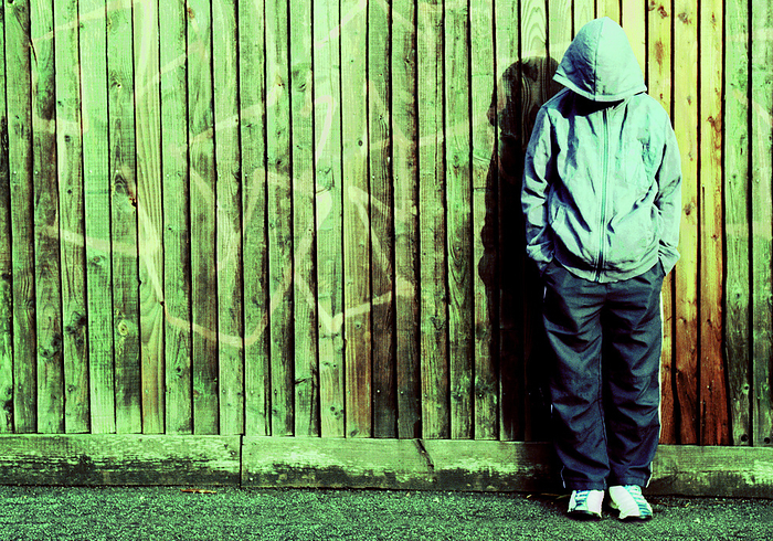 Youth crime MODEL RELEASED. Youth crime. Youth wearing a hooded jacket leaning against a vandalised fence.