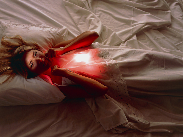 Woman awake in bed with chest or abdominal pain Night pain. Woman lying awake in bed experiencing pain in the upper abdomen or chest, represented by white and red light. She may be suffering from indigestion  dyspepsia , a general term for pain associated with eating. It typically causes a burning pain in the area behind the sternum and above the stomach. Pain resembling severe indigestion can be caused by angina pectoris, a complaint due to the heart receiving too little blood. She may also be suffering from muscular strain, a nervous disorder, or menstrual cramp.