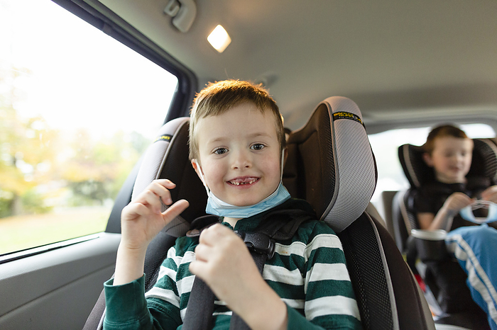 Elementary Age Boy Smiling While Sitting in Car With Face Mask