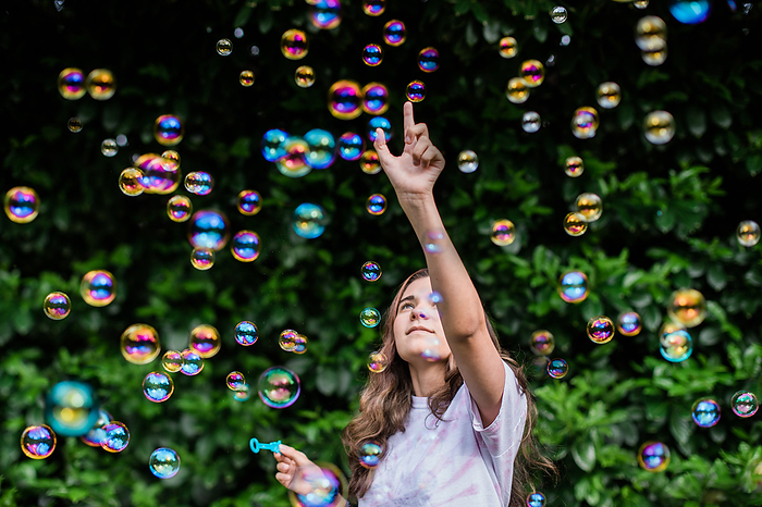 Teenager Points Up While Surrounded by Iridescent Colorful Bubbles
