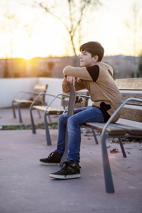 Young boy sitting on a bench holding his skateboard