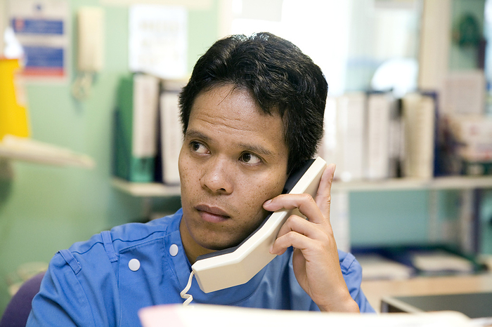 Hospital telephone use MODEL RELEASED. Hospital telephone use. Hospital staff member listening to someone talking on the telephone.