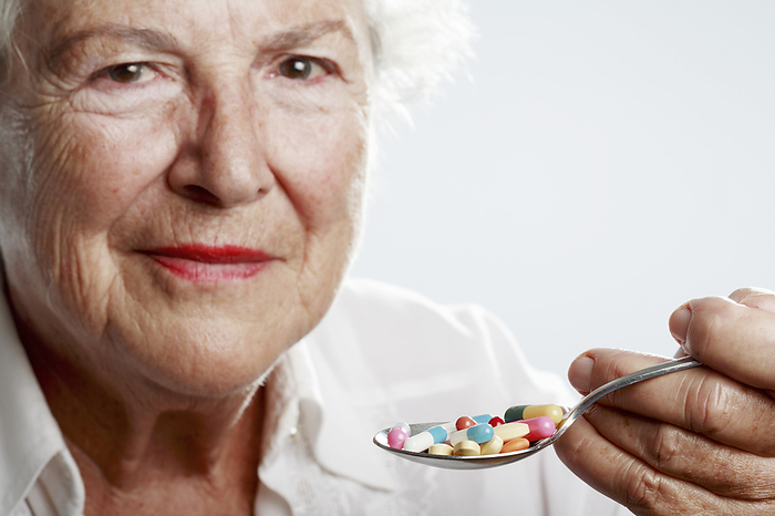 Medication MODEL RELEASED. Medication, conceptual image. Elderly woman holding a spoonful of pills.