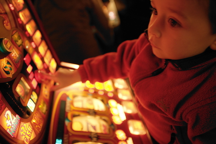 Child and gambling machine Child and gambling machine. Child being held up to look at the lights and press the buttons on a gambling machine. Gambling on gambling machines is illegal under the age of 18 years.