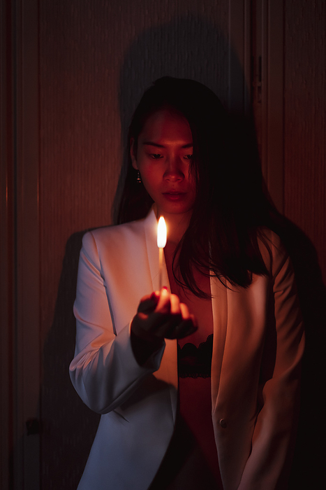female Woman wearing jacket holding burning matchstick while standing in low red light at home