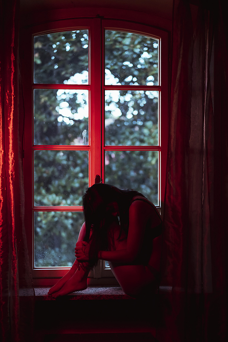 female Woman sitting with hugging knees at window sill