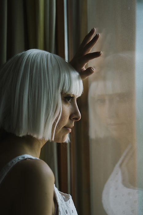 female White hair woman looking through window while standing at home, Photo by VITTA GALLERY