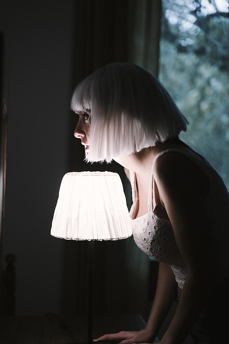 female White hair woman standing by illuminated lamp at home, Photo by VITTA GALLERY