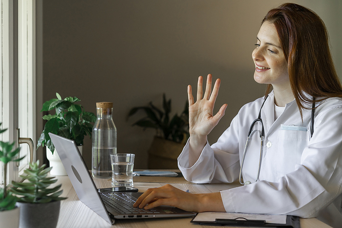 female Young female doctor waving hand at patient while providing online consultation from home office, Photo by VITTA GALLERY
