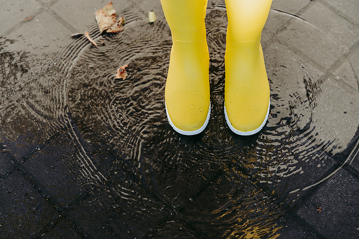 Woman wearing yellow boots standing on puddle during rainy season, Photo by Eva Blanco