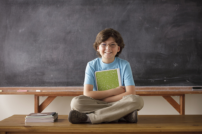   Portrait of schoolboy  10 11  cross legged sitting in front of blackboard