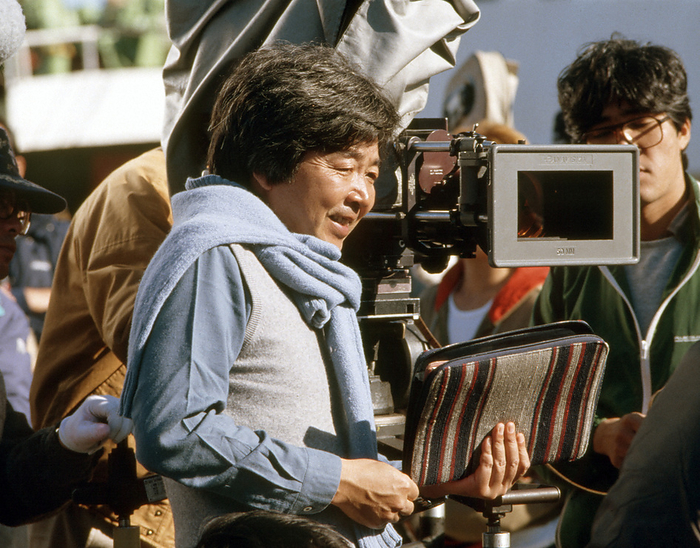 Otoko wa Tsurai yo Shibamata yori Ai wo Komete  1985   During filming . Shochiku Film s signature film, the Tora san series starring Kiyoshi Atsumi, marks its 36th installment. The setting of this year s drama is Shikinejima, Tokyo. Tora san falls in love with Komaki Kurihara, who plays an elementary school teacher on the island, which is the usual pattern. The drama will be interwoven with appearances by the islanders in the midst of the great nature. The Tora san filming is progressing smoothly, with the cooperation of the island s tourist association, and the islanders  support, including the provision of transportation vehicles and meals for the film crew, the preparation of filming equipment and props, and trash pickup. Director Yoji Yamada on location at Shikinejima for the 36th film in the  Otoko wa Tsuraiyo  series,  Shibamata kara Ai wo Komete   With Love from Shibamata , photographed by Shigeru Kimura in November 1985 at Shikinejima in Niijima Village, Tokyo.