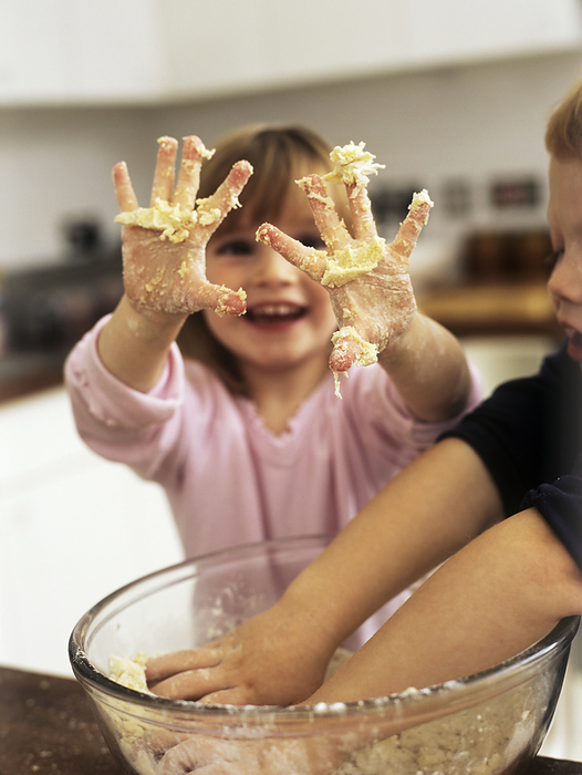 Making cakes MODEL RELEASED. Making cakes. Two three year old children mixing up the ingredients for a cake using their hands. The girl is showing off her fingers covered in the sticky egg, flour and sugar mixture.