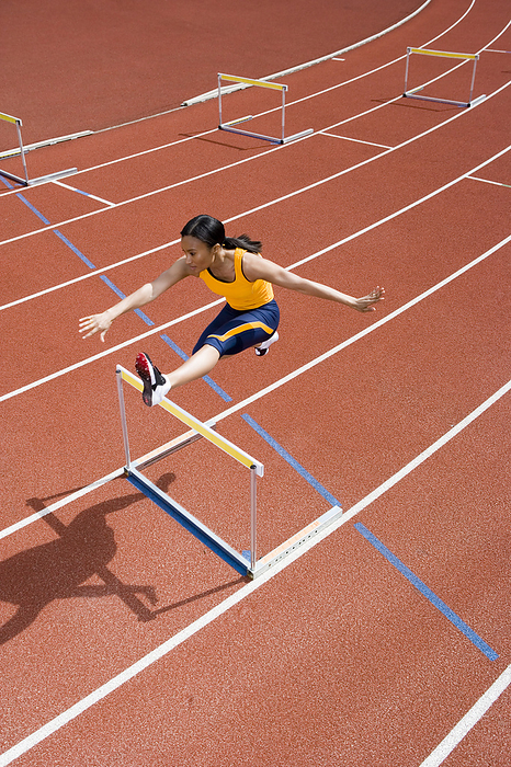 Athlete jumping over a hurdle MODEL RELEASED. Athlete jumping over a hurdle on a race track. In athletics hurdling is a track and field event. The hurdles are obstacles that the athletes jump over while sprinting down the race track. It is an event that requires both speed and excellent technique.