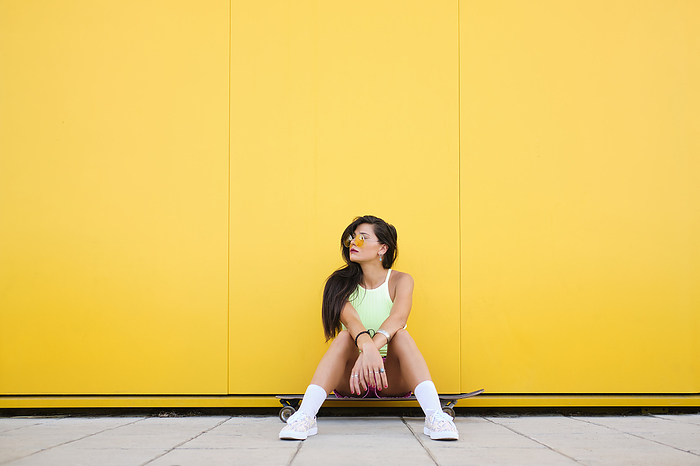 girl Portrait of beautiful girl sitting alone on longboard in front of yellow wall
