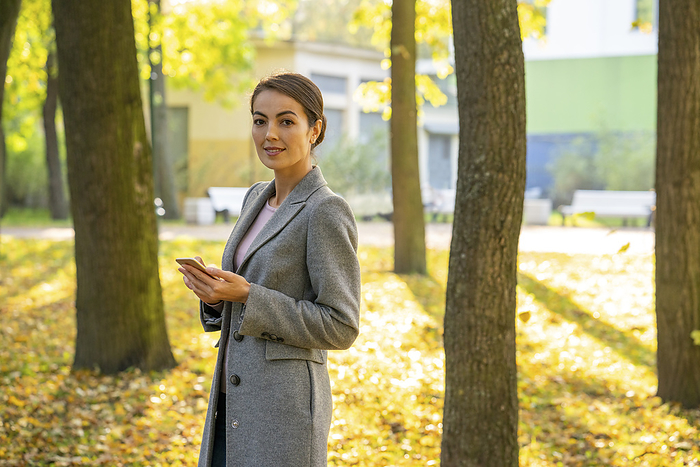 female Female entrepreneur holding smart phone in park during autumn season