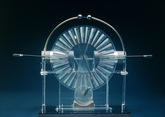 Wimshurst machine  electrostatic generator . Front view of a Wimshurst machine, a mechanical device used to generate static electricity, photographed in operation. Electrostatic charges are induced on the perimeter of 2 parallel, circular plates  appearing like windmill blades  which rotate in opposite directions when turned by a handle at bottom. Charges are collected by a system of pointed combs   stored in the tubular sections: when sufficient charge has built up, static discharge occurs across the small metallic spheres  top  in the form of a blue spark.