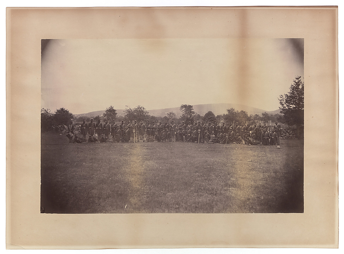 Photograph of members of the 55th Massachusetts Infantry, 1863 1865. Creator: Unknown. A photograph of 59 members of the 55th Massachusetts Infantry in uniform. The enactment of the Emancipation Proclamation by US President Abraham Lincoln on 1 January 1863 opened the way for the enlistment of free men of colour and newly liberated slaves to fight for the Union Army during the American Civil War. The image features two  2  rows of African American soldiers, with the back row of men standing and the front row of men either kneeling or lounging. The soldiers stand outside with a row of trees in the background. The image is on photo paper and has been adhered to a larger backing. The image has discoloration throughout, especially on the back. There are no inscriptions, front or back.