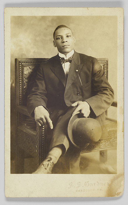 Photographic postcard of a seated man holding a bowler hat, 1904 1918. Creator: Unknown. A photographic postcard of a man seated in a wooden chair with decorative carving. His legs are crossed, and he is holding a bowler hat in his left hand. He is wearing a dress shirt, bow tie, jacket, and dress pants. There is embossed text in the bottom right corner that reads:  S. S. Gardner   BRADDOCK, PA. . The back of the photographic postcard is unused and has  POST CARD  printed in black at the top and blank spaces for  CORRESPONDENCE  and  NAME AND ADDRESS . In the upper right corner there is a  AZO  stamp.