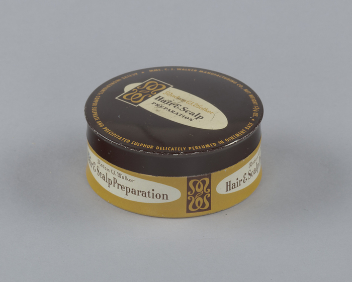 Tin for Madame C.J. Walker s Hair and Scalp Preparation, 1940s   1960s. Creator: Madam C.J. Walker Manufacturing Company. The Madam C. J. Walker Manufacturing Company, best known for its African American cosmetics and hair care products, was founded in 1910 by Madam C. J. Walker. The company is considered to be the most widely known and financially successful African American owned business of the early twentieth century. The canister is fitted to a lid that shares a similar color scheme with the main body of the container. The lid has a brown background with yellow text and at its center is a white oval formatted with the Madam CJ Walker logo on its left and the product name  Madam CJWalker Hair  amp  Scalp Preparation  written in brown text. The canister has a yellow background with brown text  the side label has a slightly larger white oval than the oval on the lid. It is framed on either side by the Madam CJ Walker logo. The product name is written in brown text in the oval on the can side and reads  Madam CJ Walker Hair  amp  Scalp Preparation .