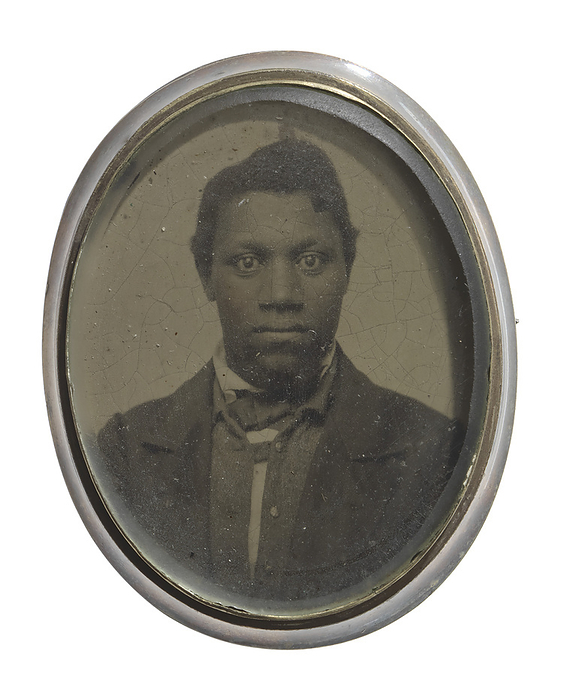 Brooch with a portrait of an unidentified man, ca. 1860. Creator: Unknown. Ladies  oval shaped brooch with a black and white tintype photograph of an African American man. The brooch is silver in color with a glass front and a pushpin back. The man in the photograph is wearing a dark colored necktie, jacket and vest with a white shirt.