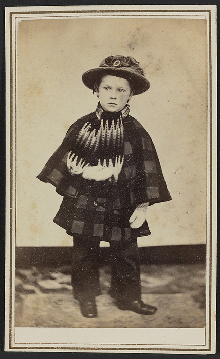 Carte de visite portrait of Willy Hall, ca. 1860. Creator: Unknown. Carte de visite of William Woodhull  quot Willy quot  Hall in full length standing portrait. Hall wears a round brimmed hat with a feather and buckle on the front of the band, a white and black zigzag patterned scarf tied around his neck, a plaid inverness coat that falls mid thigh, white mittens, long dark pants, and dark shoes with round toes. His left hand hangs at his side, while his right is held in front of his chest. He faces the camera but is looking off to his right. There is a double lined border printed in gold ink surrounding the outside edges of the card mount. The photograph is housed in the album 2017.30. The album page has a triple lined, gold border framing the print. Handwritten in graphite in the bottom of the printed frame of the window on the album page with this photograph is the text  quot Willy Hall died 1864   at Camp Distribution Va. quot  William Hall was the son of Maria Miller Woodhull Hall  1831 1913  of Jamestown, New York, and William Charles James Hall  1828 1887  a major of the 23d U.S. Colored Troops.