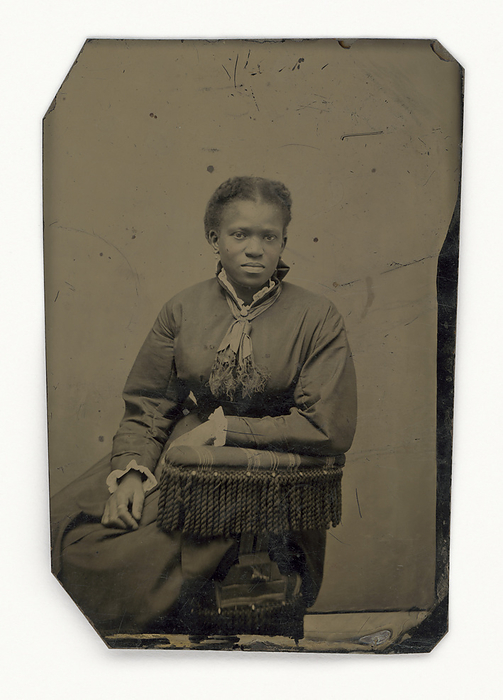 Tintype of a woman, late 19th century. Creator: Unknown. An unidentified African American woman sitting on a chair and leaning on the chairback with her left forearm. She wears a longsleeved dress with a neck scarf.