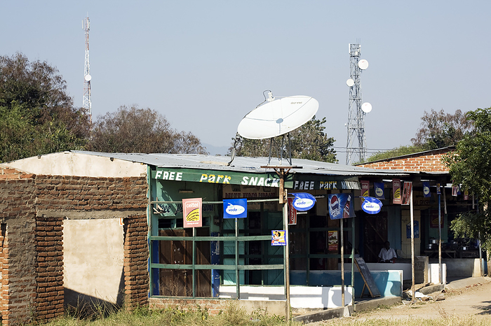 Telecommunications dish and mast, Africa Telecommunications dish and mast. Satellite dish on the roof of a shop beside a telecommunications mast. Advertising for Vodacom and Celtel mobile phone companies is displayed in shops and restaurants. Mobile phone communication networks operate by the transmission of radio signals between mobile phones and base stations. The dishes and antennas on these masts receive, amplify and relay mobile phone, microwave and radio signals. Photographed in Mikumi, Tanzania, Africa.