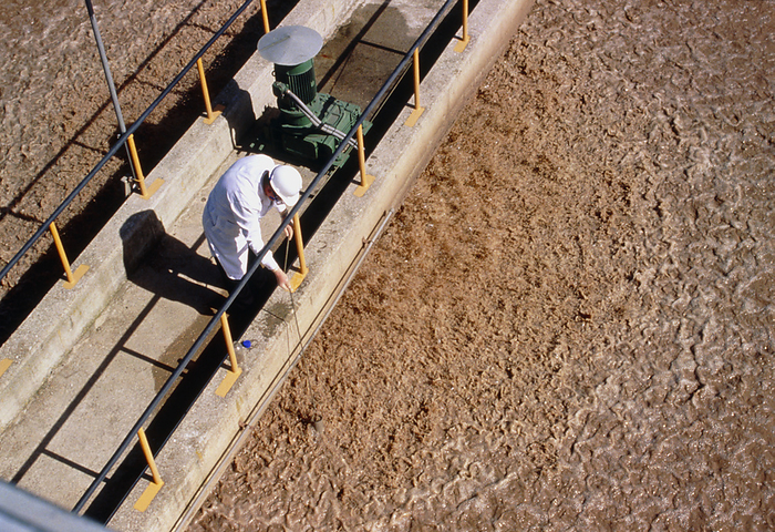 Technician taking sample at water treatment plant Water treatment plant. A technician taking a water sample from a bridge at a water treatment plant.