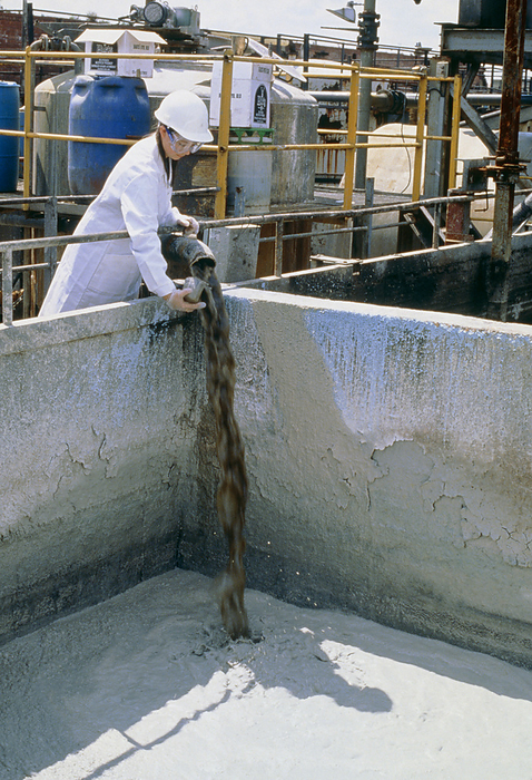 Chemist sampling chemical waste for toxicity Chemist taking a sample from a stream of industrial waste slurry to test for toxicity at a chemical waste treatment plant.